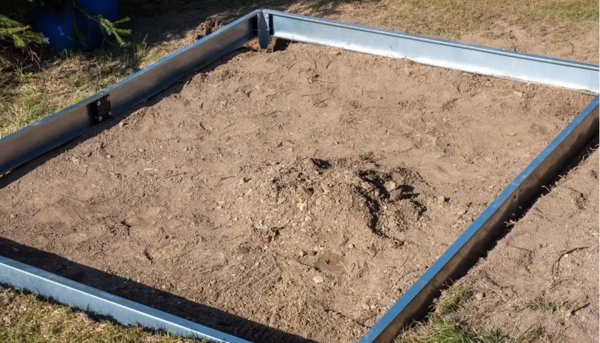 Metalowa rama na ziemi, gotowa na zrobienie fundamentu pod szklarnię.