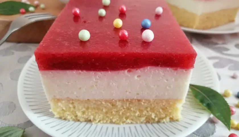 Pyszna żelka truskawkowa z mrożonych truskawek, z kremową warstwą i biszkoptem, ozdobiona kolorowymi kuleczkami.