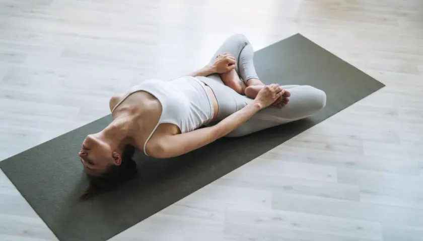 Kobieta w pozycji supta baddha konasana na macie do jogi, relaksująca biodra i pachwiny.