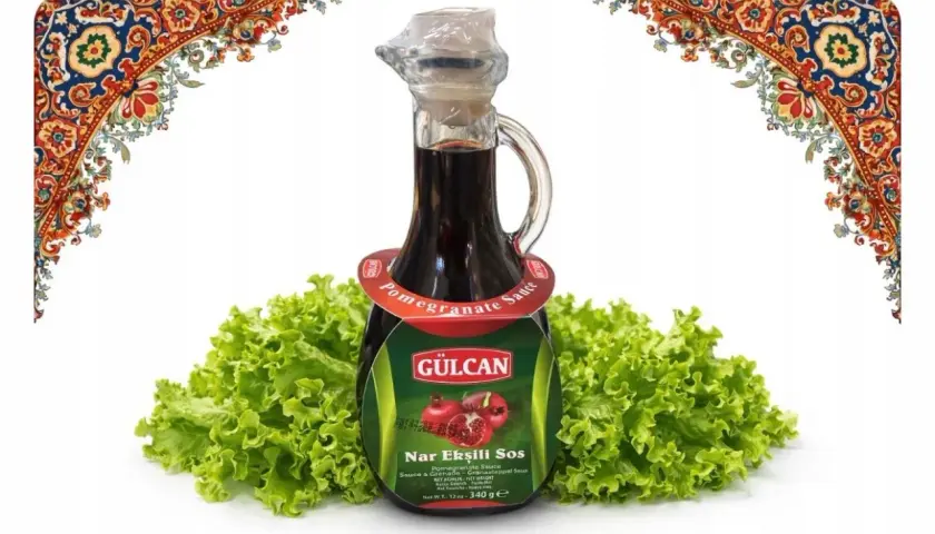 Butelka sosu z granatu Nar Ekşili Sos na tle sałaty, ozdobiona orientalnymi wzorami.