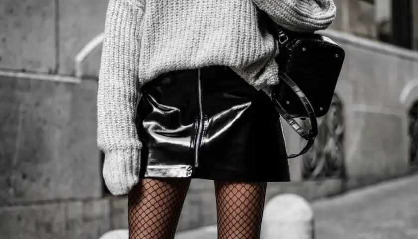 Une idée tenue avec collant résille : jupe vinyle noire, pull gris oversize et sac structuré.