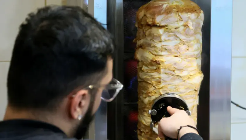 Mężczyzna kroi mięso z pionowego rożna na kebab.