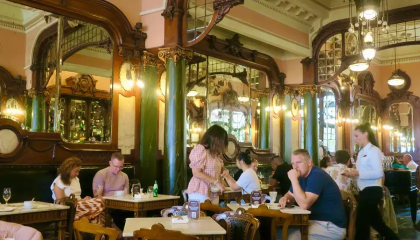 Interno di un **majestic cafe porto** con arredi d'epoca, specchi e clienti seduti ai tavoli.