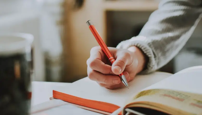 Main d'une personne écrivant avec un stylo rouge dans un carnet, un sujet d'écriture spontanée.