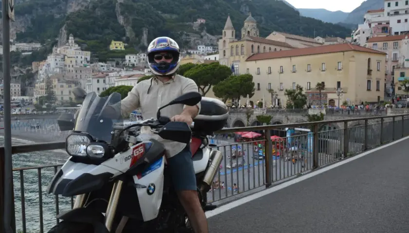 Motociclista in sella alla sua BMW, ammira il panorama della meta costiera amalfitana con le case aggrappate alla montagna.
