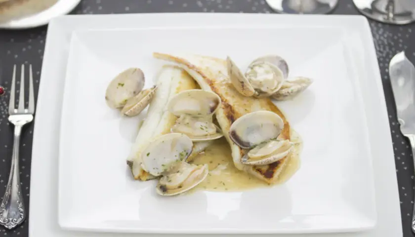 Coruxo pescado con almejas en salsa cremosa, servido en plato blanco.