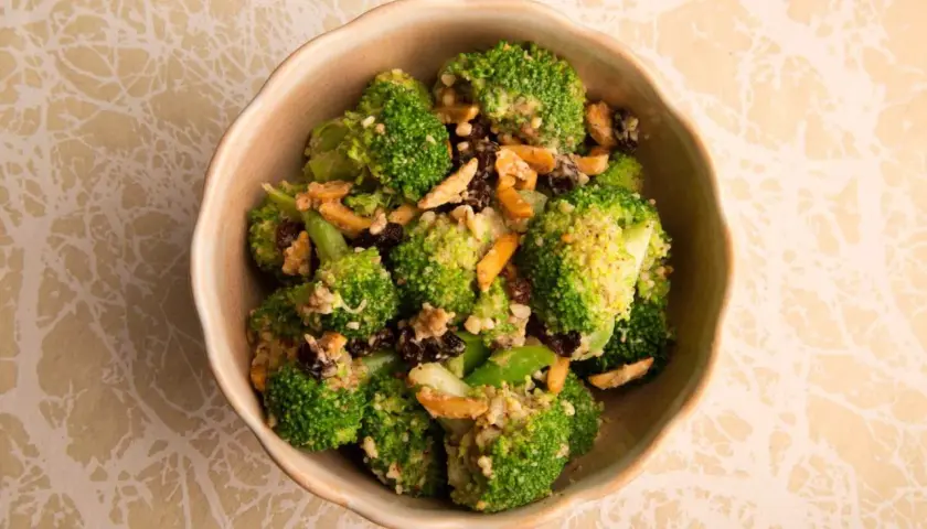 Ensalada de brócoli fresca con pasas y nueces, servida en un cuenco de cerámica.