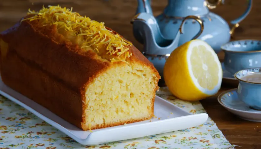 Puszysta babka cytrynowa, ozdobiona skórką cytrynową, czeka na herbatę z błękitnego serwisu.