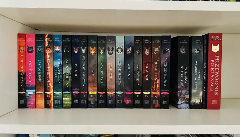Półka z książkami dla 5 latka, seria Wojownicy Erin Hunter. Kolorowe okładki z kotami i tytułami jak "Ucieczka w dzicz".