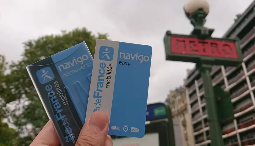 Dłoń trzyma paryskie karty Navigo na tle znaku metra.