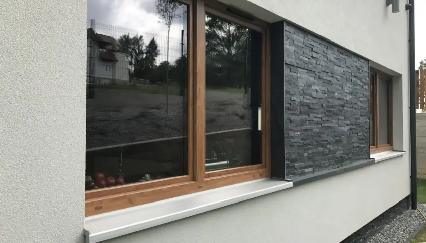 Nowoczesne okna z drewnianymi ramami i kamiennymi opaskami wokół okien, odbijające niebo i otoczenie.