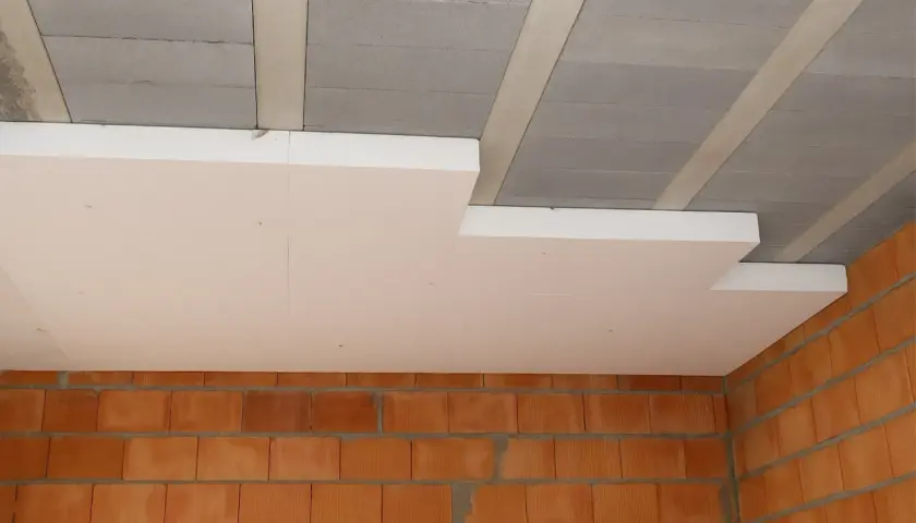 Ocieplenie stropu styropianem w trakcie budowy. Widoczne betonowe pustaki stropowe, płyty styropianowe i ściana z cegły.