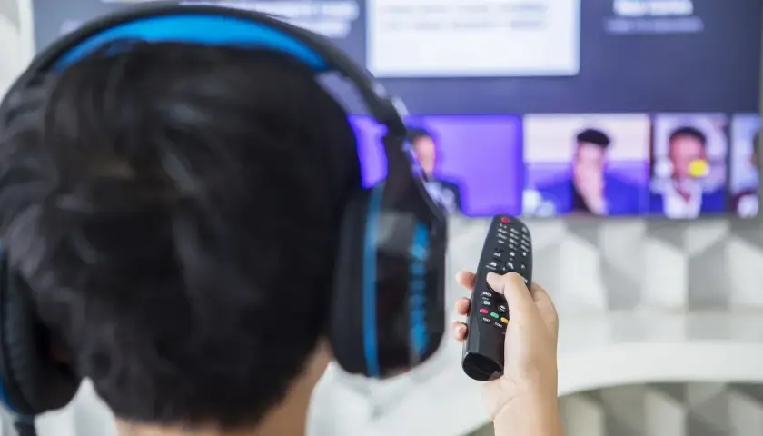 Chłopak w słuchawkach z pilotem w ręku, gotowy do oglądania na telewizorze Samsung. Dowiedz się, jak podłączyć słuchawki do Samsunga, by cieszyć się dźwiękiem.