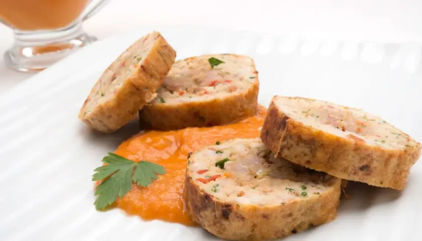 Rollo de bonito cortado en rodajas, servido sobre puré de pimientos y decorado con perejil.
