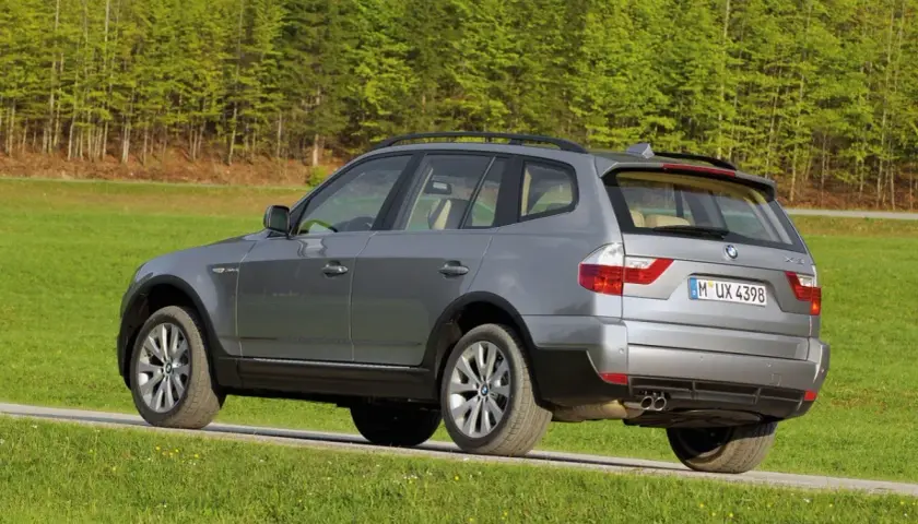 Szary BMW E83 na tle zielonego lasu i łąki.