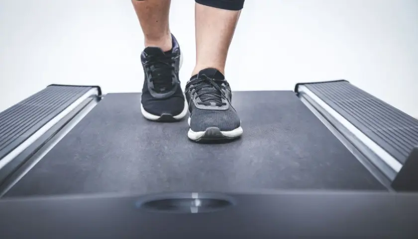 Nogi w sportowych butach stawiają pierwsze kroki na bieżni w bloku.