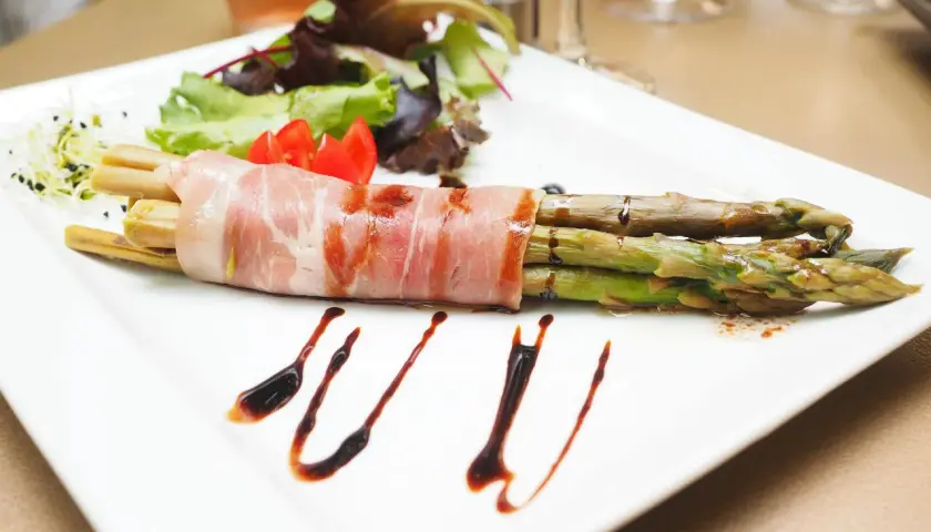 Zielone szparagi owinięte szynką parmeńską, podane z sałatką i sosem balsamicznym.