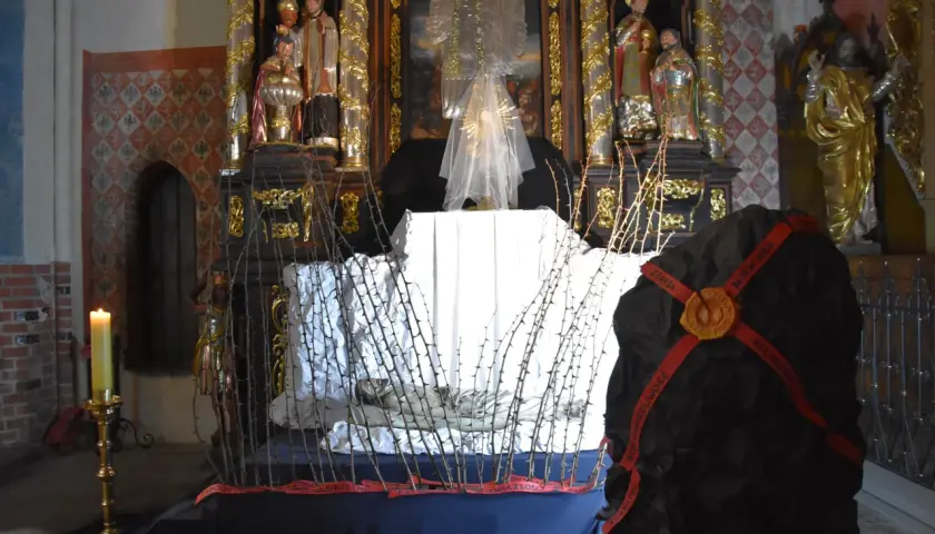 Ołtarz w kościele z grobem Chrystusa, ozdobiony ciernistymi gałęziami i świecą.