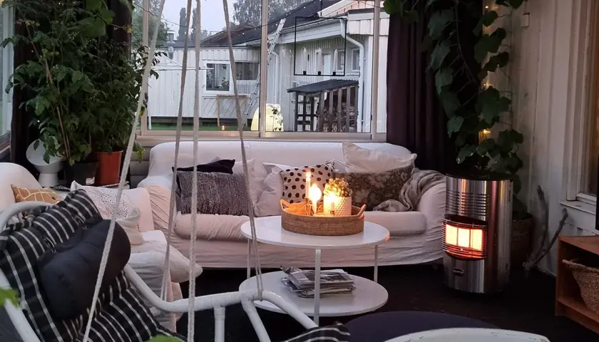 Mysig stuga inredning med soffa, korgstol, växter och tända ljus. En gasolkamin ger värme.