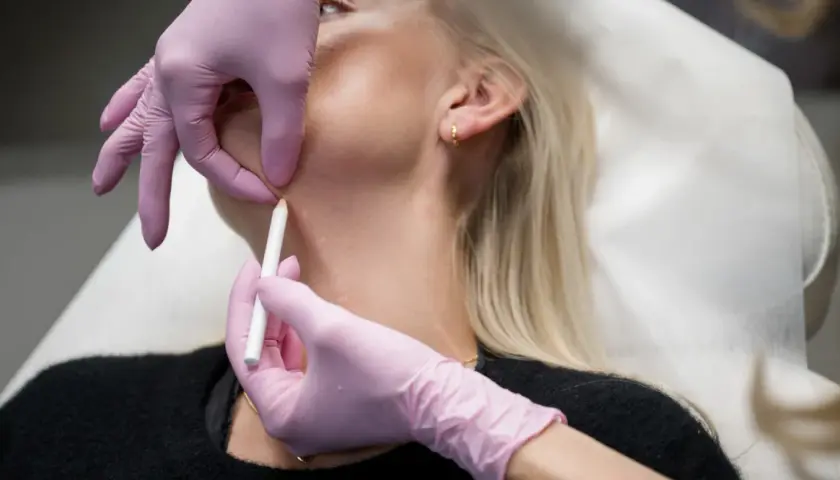 En person får botox i nacken. En hand med rosa handske markerar med en penna på huden.