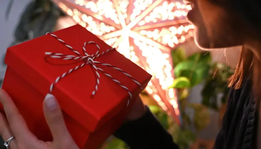 Ein rotes Weihnachtsgeschenk in Händen, im Hintergrund ein leuchtender Stern.