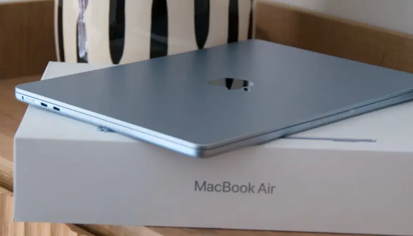 MacBook Air azul cerrado sobre su caja, con un jarrón al fondo.
