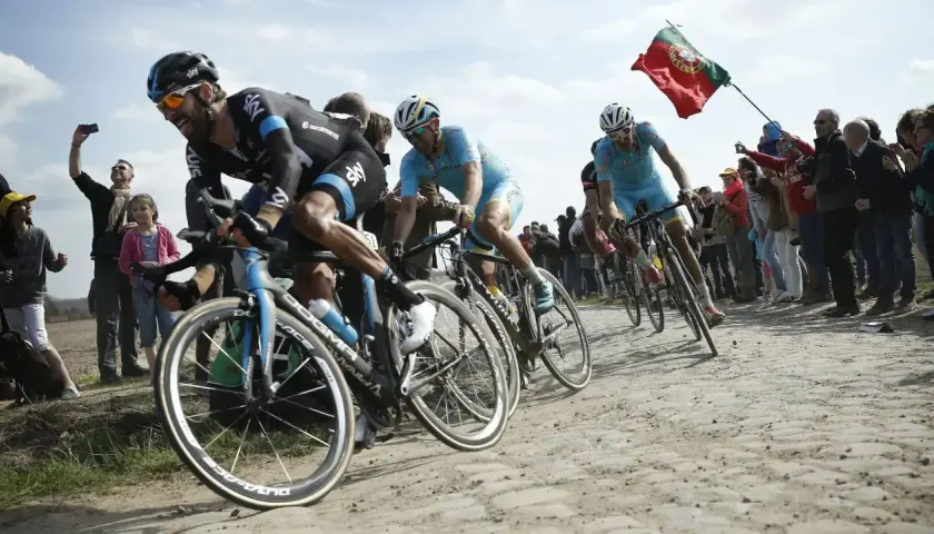 Radprofis kämpfen auf Kopfsteinpflaster, ein portugiesisches Banner weht. Ein Moment, der die Härte und den Ruhm der monumente des radsports einfängt.