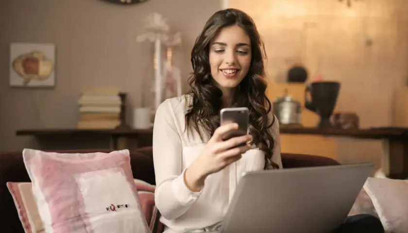 Uśmiechnięta kobieta z telefonem i laptopem, planuje zakupy, korzystając z erli metody płatności.