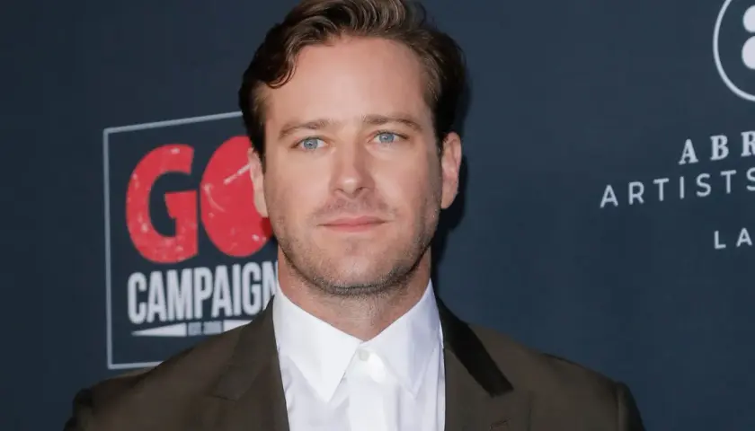 Armie Hammer, med sina blå ögon och mörk kostym, poserar framför en bakgrund med texten "GO CAMPAIGN".