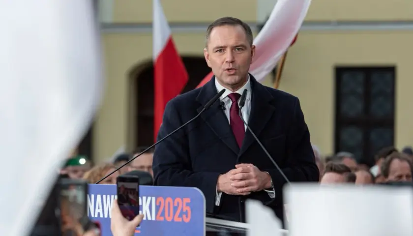 Polityk przemawia na tle flag. Na banerze widnieje napis "NAWROCKI 2025".