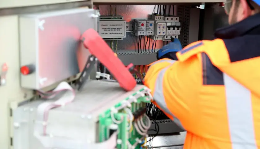 Elektryk w pomarańczowej kamizelce pracuje przy panelu sterowania, podłączając kabel neutralny.