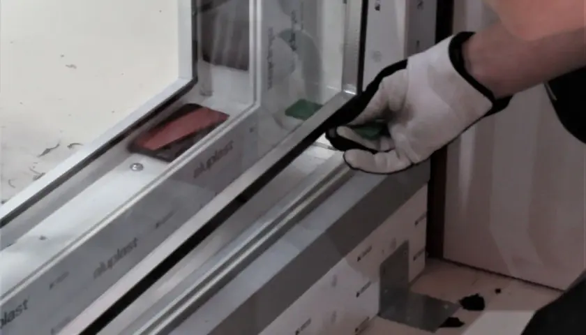Rękawica montażysty umieszcza zieloną podkładkę pod szybę termoizolacyjną w ramie okiennej.