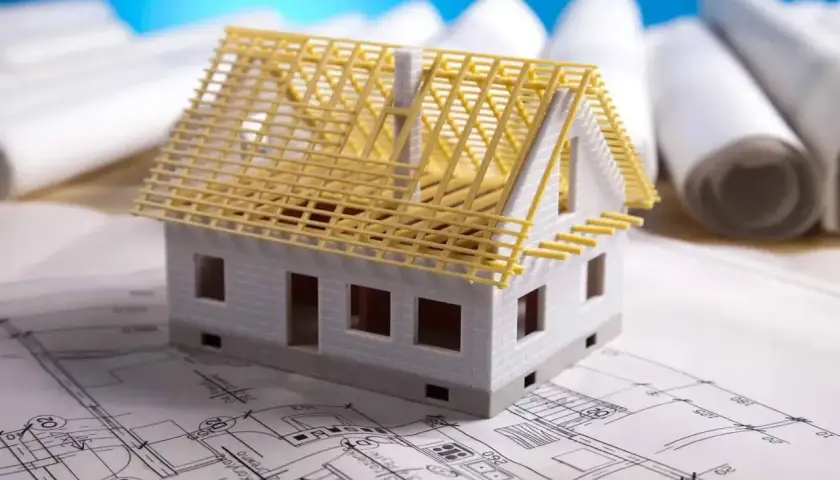 Model domu na planach architektonicznych, z widoczną konstrukcją dachu. Zastanawiasz się, ile kosztuje adaptacja projektu?