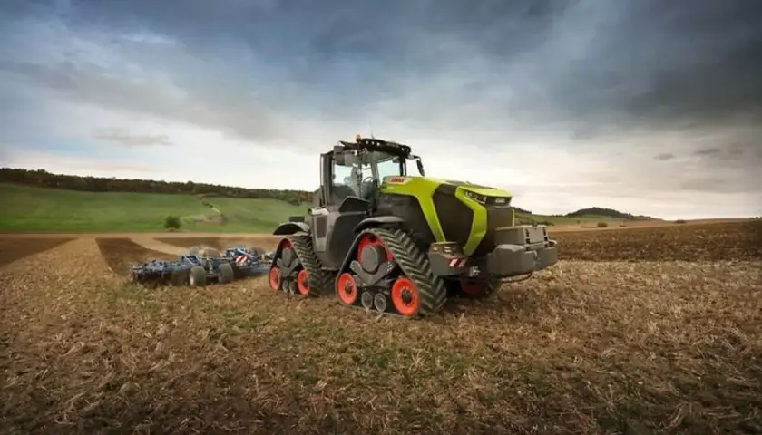 Potężny Claas Xerion z gąsienicami pracuje na polu, przygotowując ziemię do siewu.