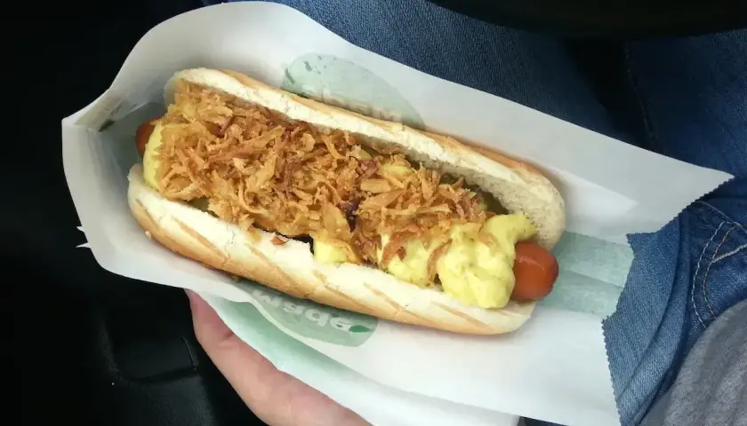 Pyszny hot dog z chrupiącą cebulką i sosem, idealny na szybki posiłek. Gdzie kupić sosy z Orlenu? Warto sprawdzić na stacji!