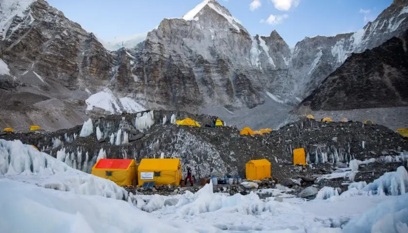 Obóz u podnóża Mount Everest, gdzie **mount everest wysokość** jest wyzwaniem. Żółte namioty na lodowcu, w tle majestatyczne, skaliste szczyty.