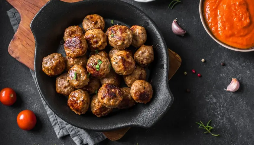 Polpette dorate e succulente, cotte alla perfezione nella friggitrice ad aria, pronte per essere gustate con salsa e pomodorini freschi.