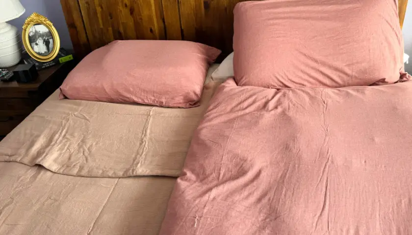 A bedspread can be used as a blanket, as shown by this cozy, pink-covered bed with a wooden headboard.