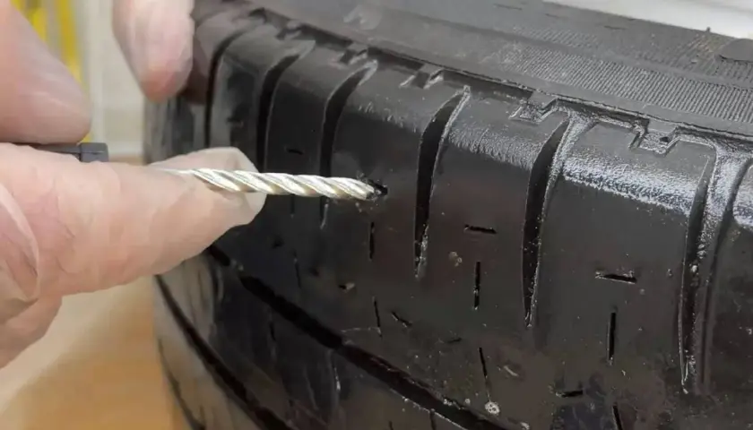Manos con guantes reparando un pinchazo en un neumático con una herramienta.