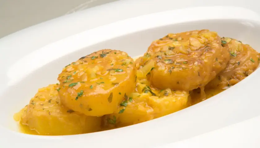 Patatas a la importancia, doradas y jugosas, bañadas en una salsa con ajo y perejil, servidas en un plato blanco.