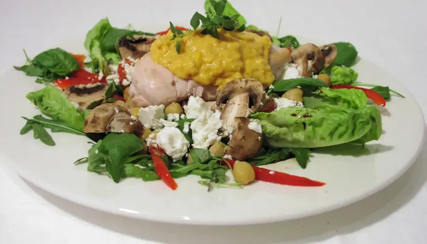 Chicken salad with mushrooms, feta cheese, chickpeas, red pepper, and greens on a white plate.