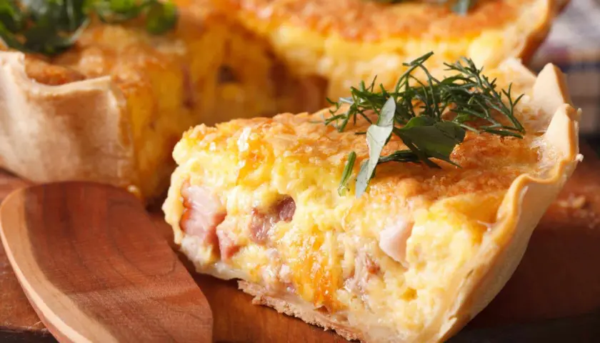 Une part de quiche raclette, garnie d'herbes fraîches, sur une planche en bois. Un délice gourmand !