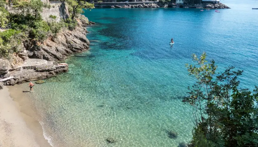 Un homme profite de ses vacances à Portofino, se baignant dans les eaux cristallines. Une personne fait du paddleboard au loin.