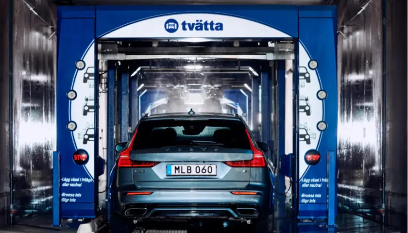 En Volvo är på väg in i en biltvätt. Vatten sprutar och underspolning av bilen pågår.