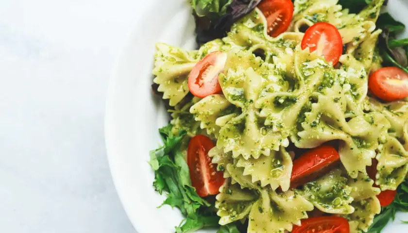 Ein köstlicher italienischer Nudelsalat mit Farfalle, Pesto und Kirschtomaten, garniert mit frischem Salat.