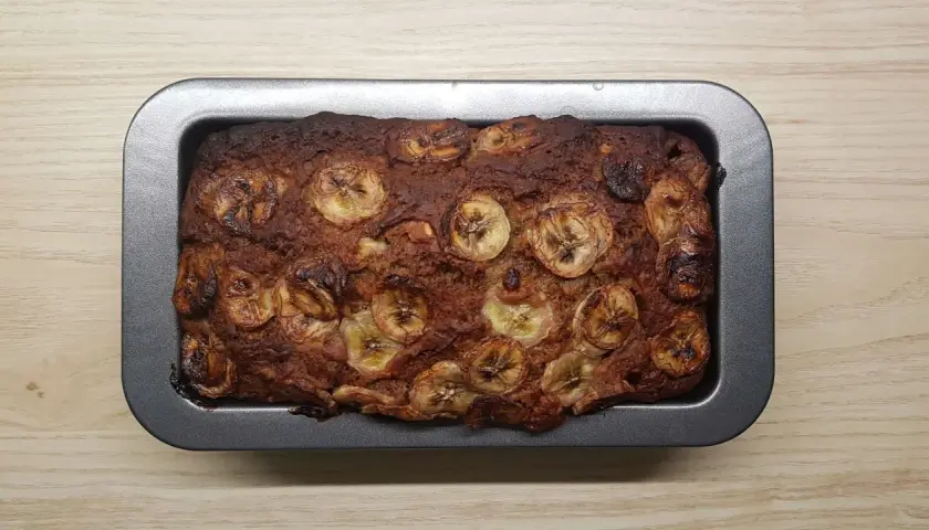 Upieczony proteinowy chlebek bananowy z plasterkami banana na wierzchu, w metalowej formie.