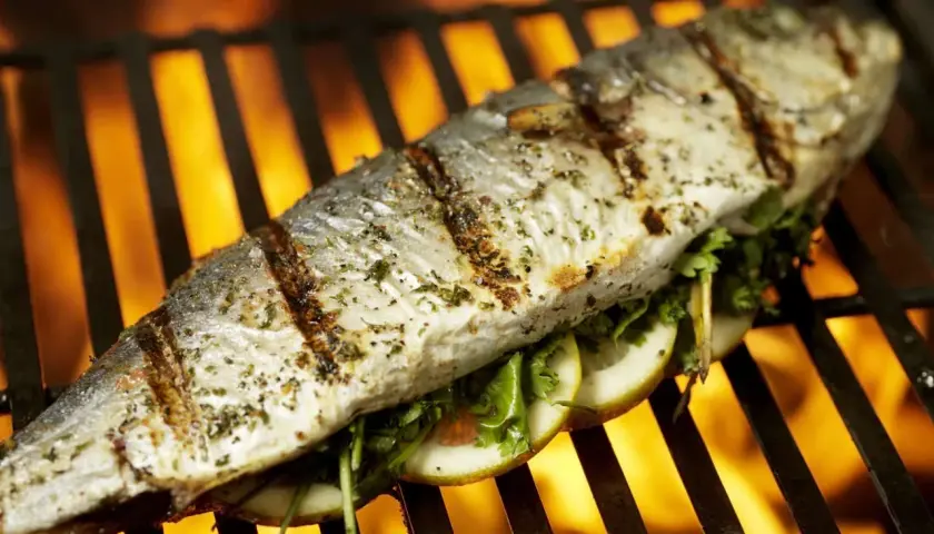Poisson entier assaisonné, garni de tranches de citron et d'herbes, cuisant sur un gril avec des flammes vives en arrière-plan. Un délice de thon au barbecue.
