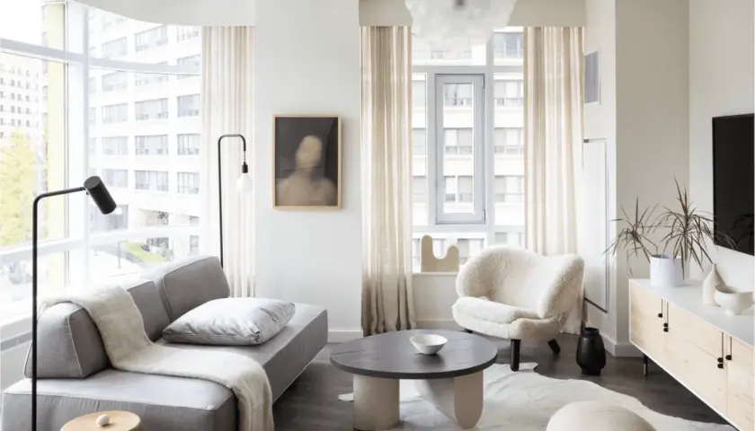 A cozy living room, perfect for learning how to furnish a small apartment. A grey sofa, fluffy armchair, and round coffee table create a welcoming space.