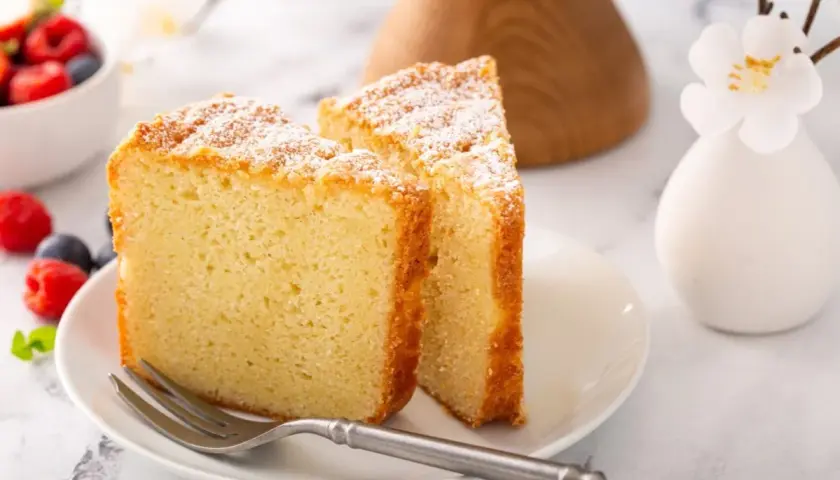 Dos porciones de pa de pessic, esponjoso y espolvoreado con azúcar glas, junto a frutos rojos y un tenedor.