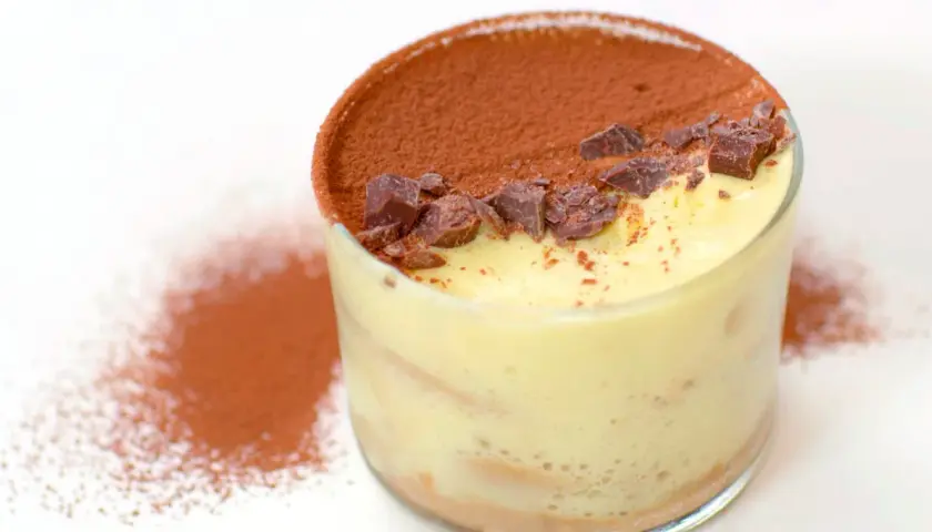 Delizioso tiramisù fatto in casa in un bicchiere, cosparso di cacao e scaglie di cioccolato.